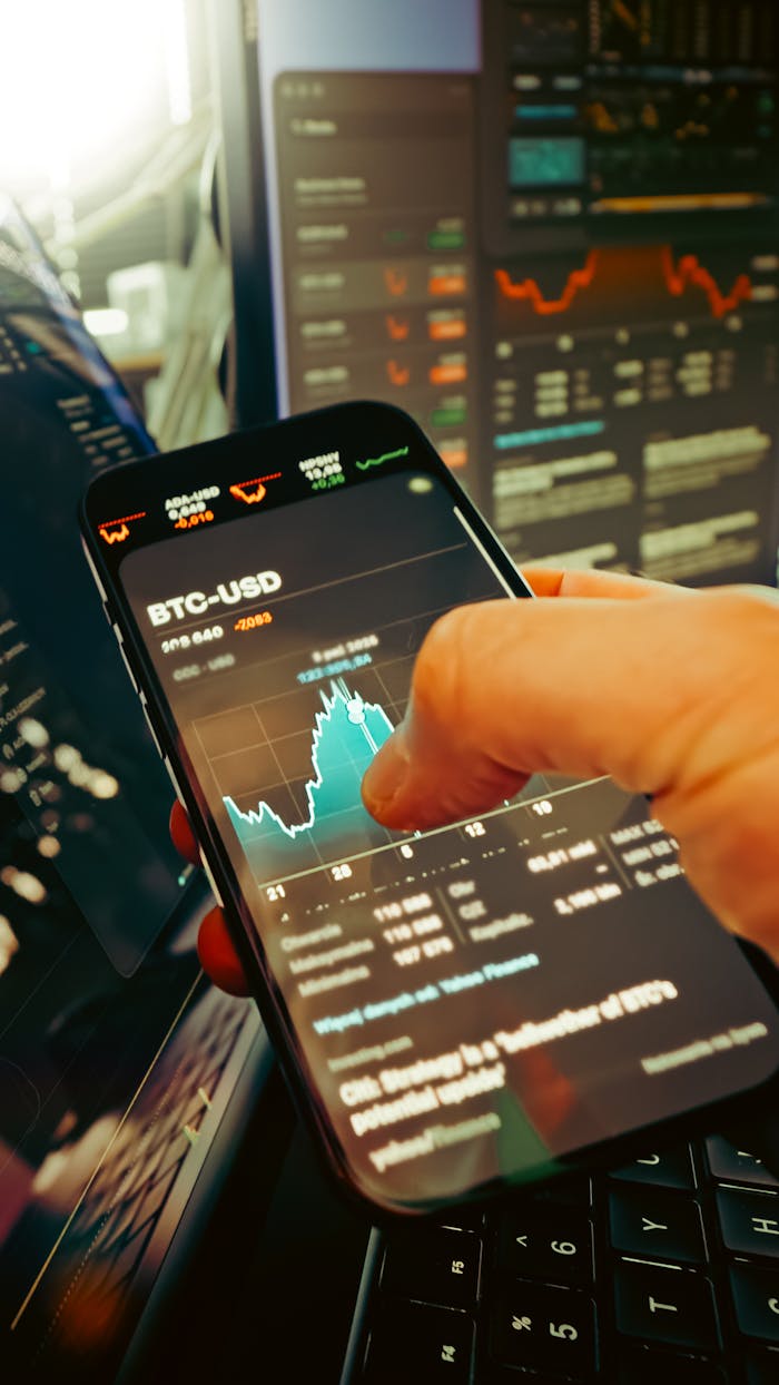 services-01 A hand holds a smartphone displaying BTC-USD chart amidst digital trading screens, highlighting crypto finance.